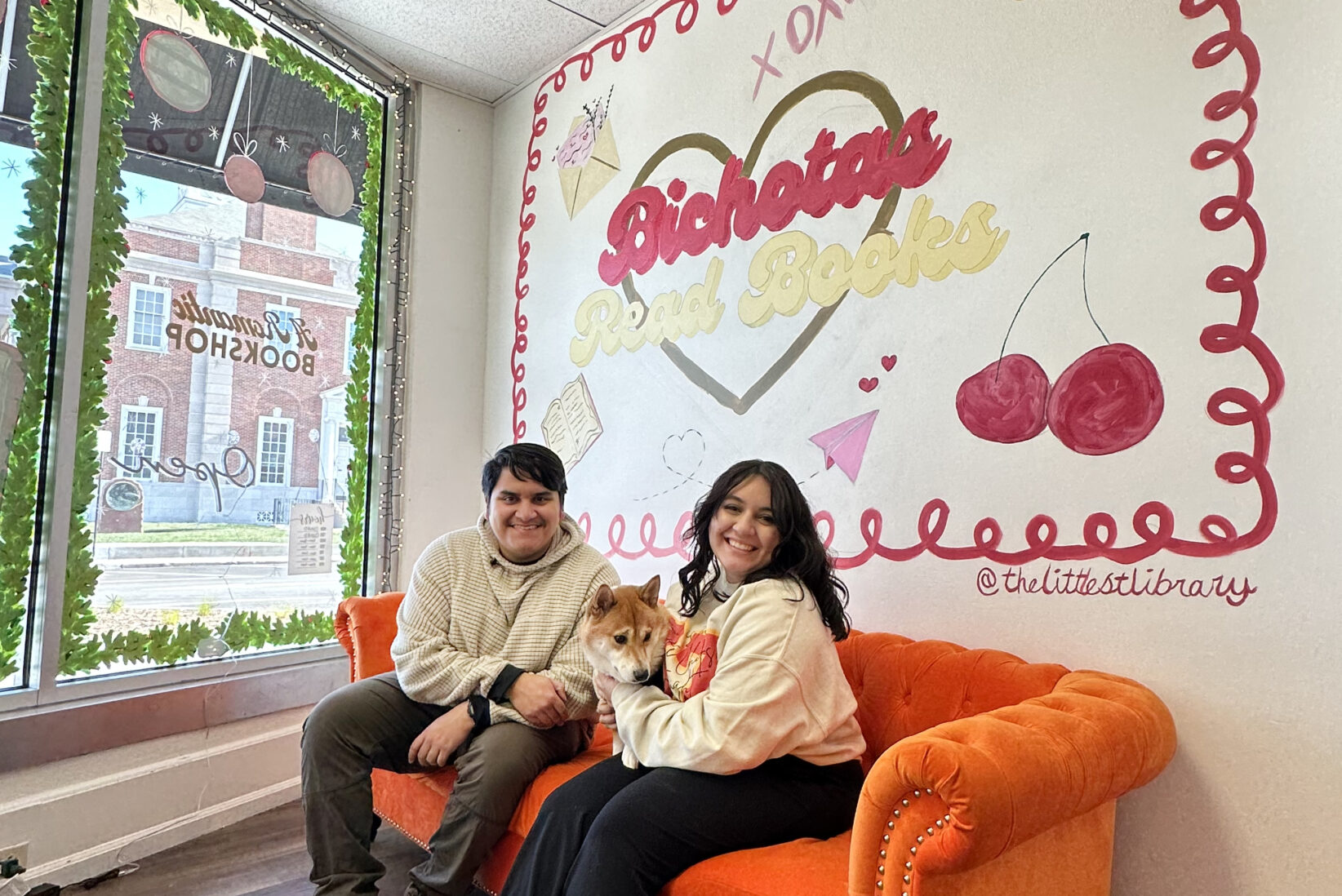 America Fontenot, right, sits inside The Littlest Library at 112 N. Liberty St. on Independence Square, alongside her fiancé Edgar Cerna and their 3-year-old Shiba Inu. Fontenot and Cerna have been dating since middle school, their own romance behind the scenes at the new bookstore; photo by Joyce Smith