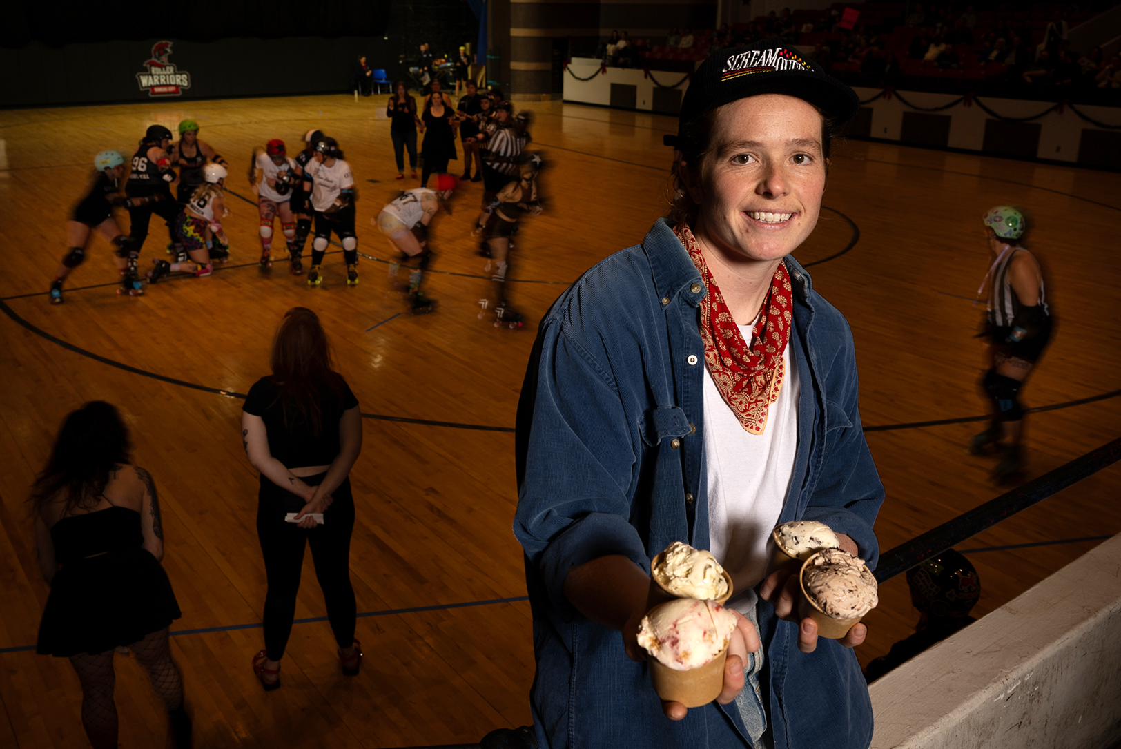 With the roller derby bout underway, Zoe Mays of Scream Queens vegan ice cream, a resident concession partner at the event, posed with the four special flavors she developed in partnership with the teams. The Kansas City Roller Warriors bout wast at Memorial Hall in Kansas City, Kansas on Dec. 6, 2025; photo by Todd Feeback, Flatland