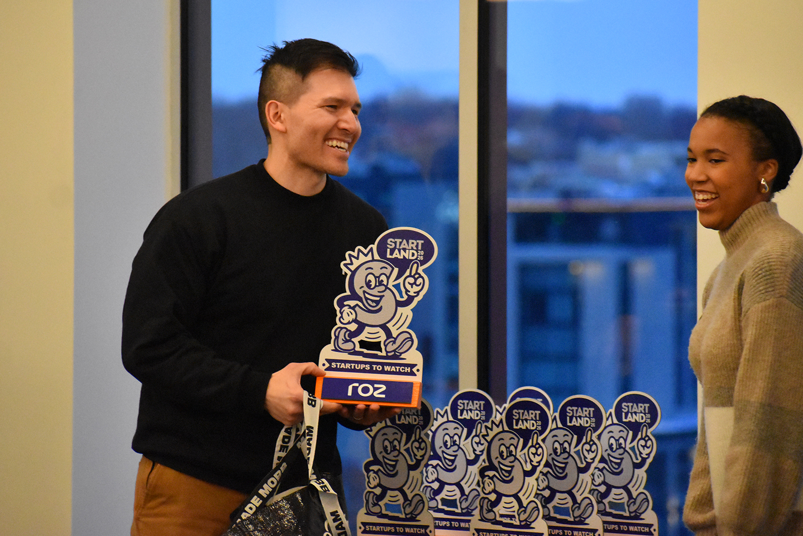 Donnie Hampton, co-founder of Roz, accepts his Kansas City Startups to Watch in 2026 trophy — featuring Startland News' mascot, Scoop — from Startland News reporter Taylor Wilmore during an awards reception for the companies at Husch Blackwell's Kansas City headquarters on the Country Club Plaza; photo by Tommy Felts, Startland News