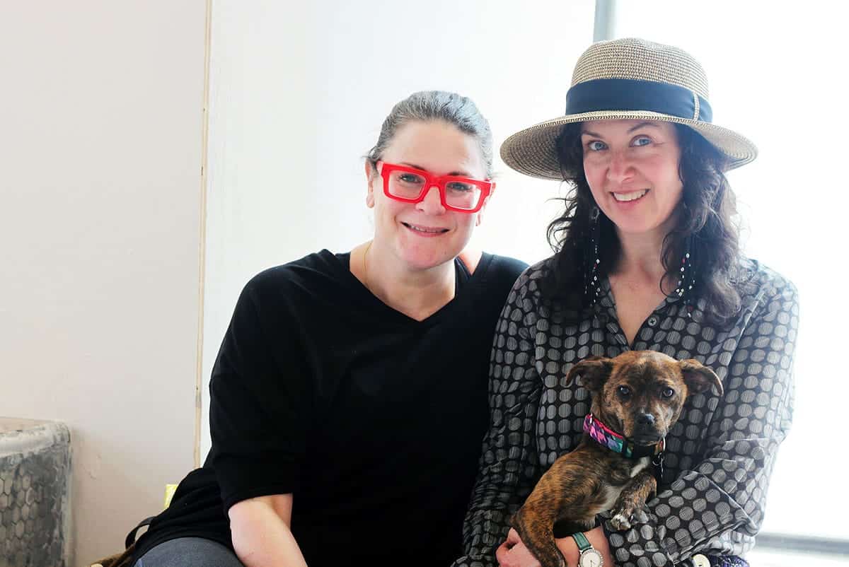 two women smiling at camera while holding a dog