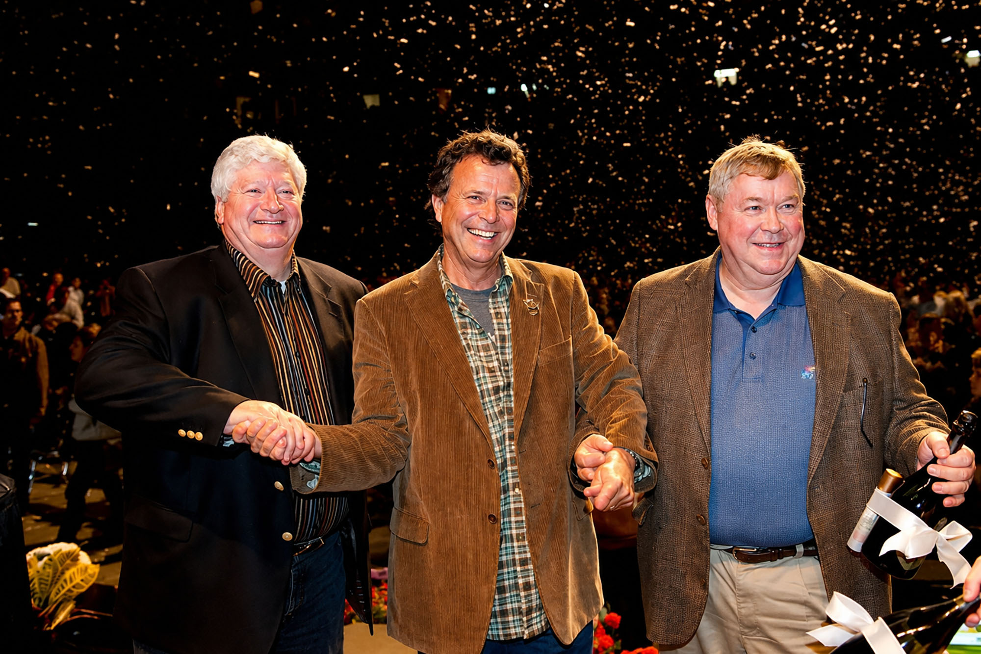 Cerner co-founders Cliff Illig, Neal Patterson, and Paul Gorup clasp hands at a 2009 celebration of Cerner’s 30th anniversary; photo by Steve Puppe, courtesy of the Patterson Family Foundation