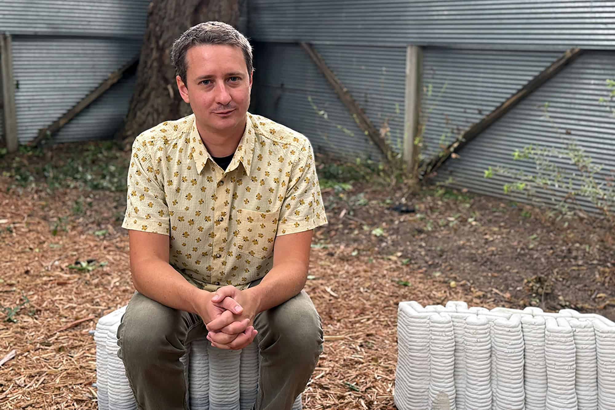 Reese Greenlee, K-State assistant professor of architecture, sits on a 3D-printed concrete building block; photo courtesy of Kansas State University