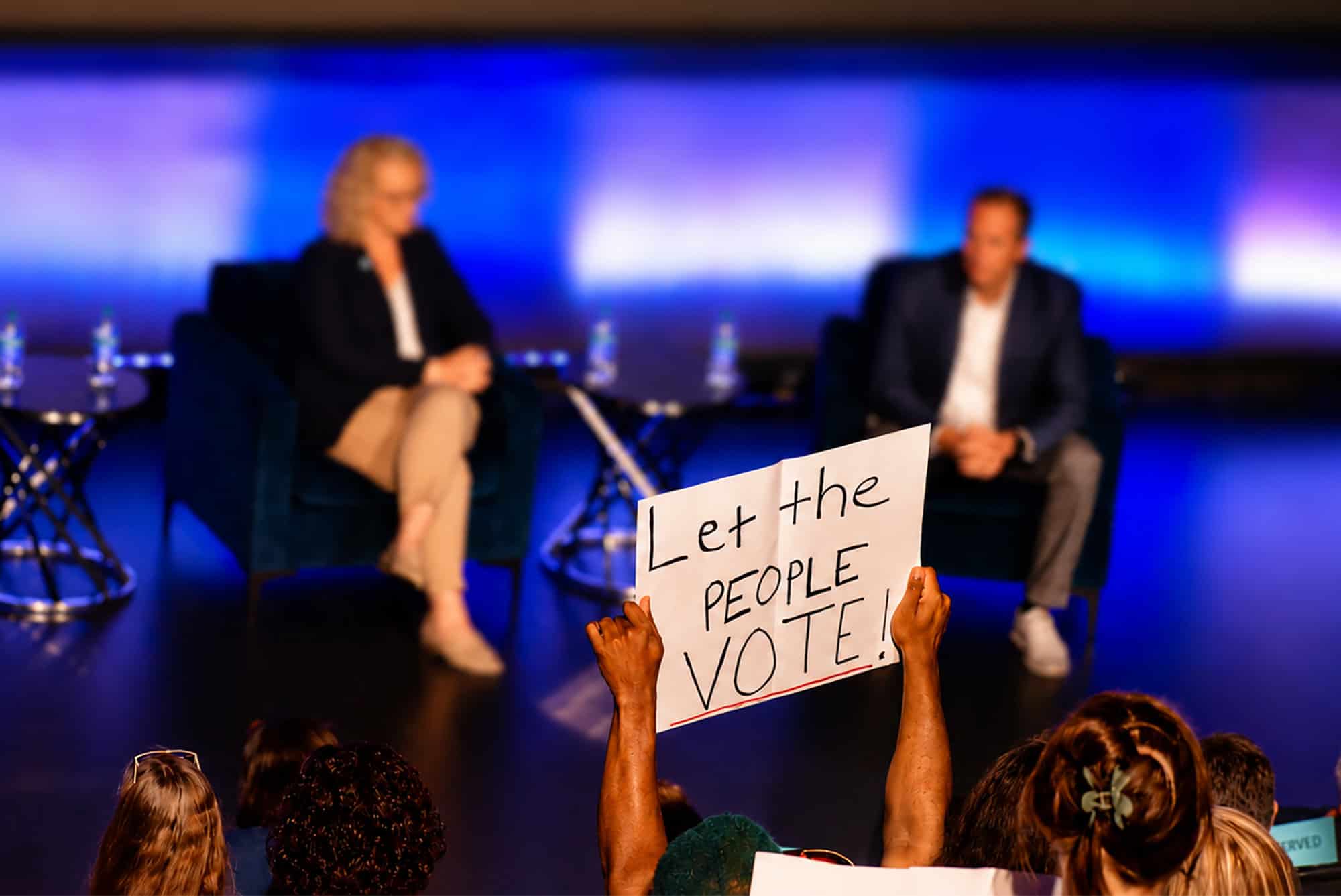 A critic of the Royals' plan to build a stadium at Crown Center holds a "Let the People Vote" sign during a public meeting in the Regnier Theatre at Union Station; photo by Nikki Overfelt Chifalu, Startland news